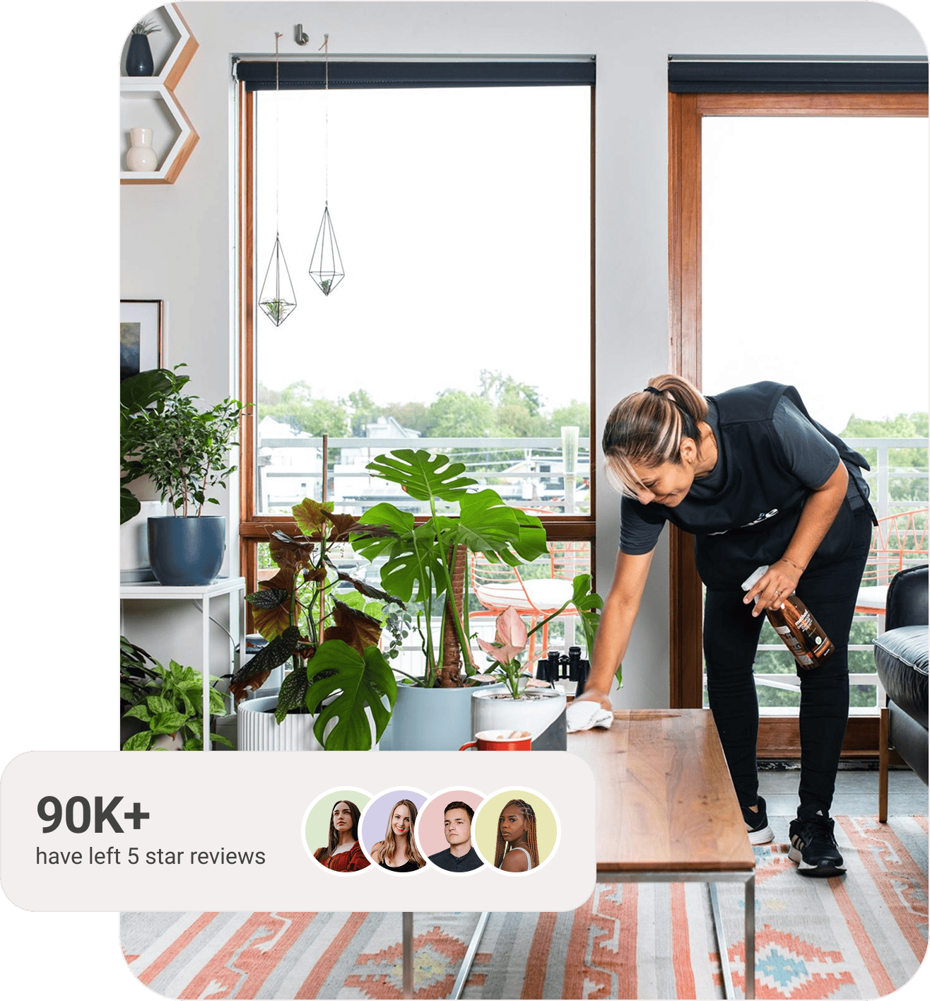A professional cleaner wipes down a wooden coffee table in a bright, modern living room filled with green houseplants and natural light from large windows. A text overlay in the corner reads “90K+ have left 5-star reviews,” accompanied by profile icons of four diverse people representing satisfied Spruce customers.
